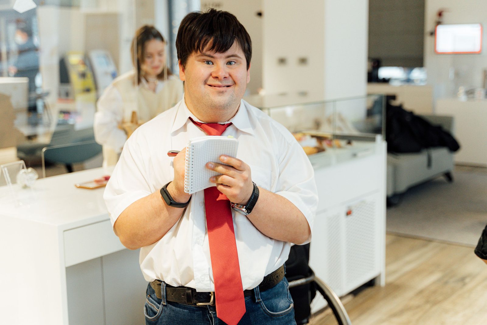 A man with Down syndrome in a white shirt and red tie writes in a notebook.